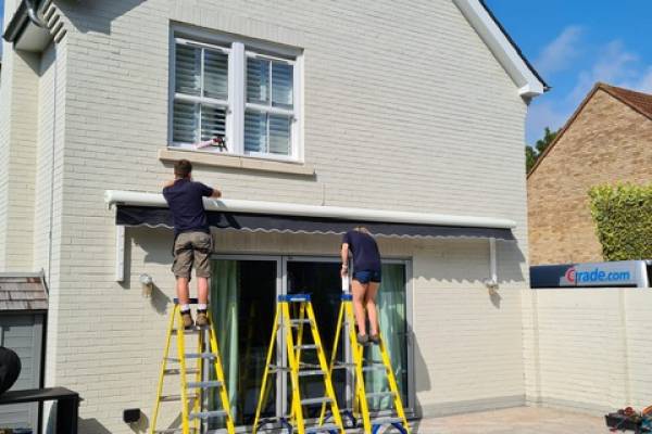 Photo of two engineers from Advance Shutters fitting an awning to a house.